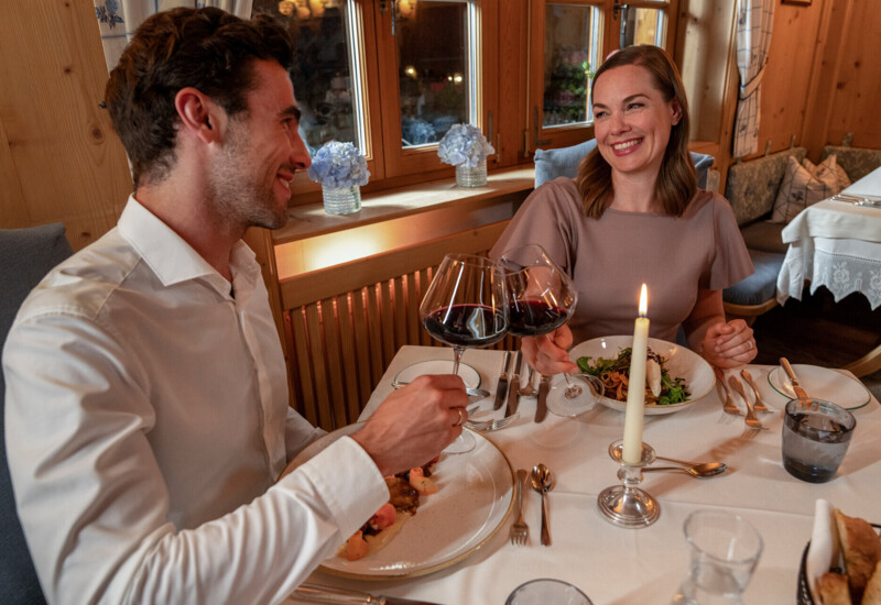 A couple enjoying a candlelit dinner with wine at a cozy, wood-paneled restaurant.