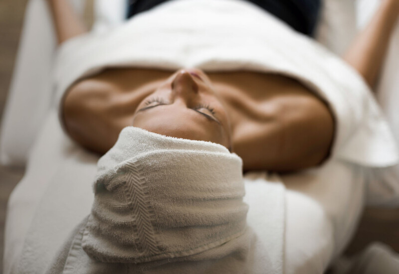 A person relaxing on a spa table with a towel wrapped around their head, creating a serene atmosphere.