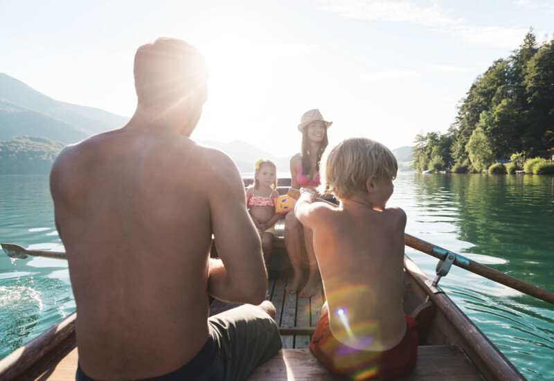 A family enjoys rowing on lake Fuschl, surrounded by lush green forests and scenic mountains.