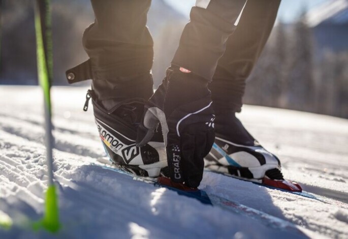 Langläufer schnallt Ski auf verschneitem Gelände an, mit Skistöcken im Vordergrund.