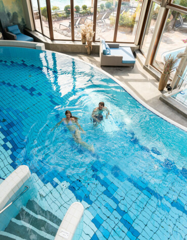 Pärchen beim Schwimmen im großzügigen Innenpool des 4*S Wellnesshotel Waldhof Fuschlsee Resort