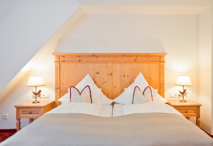 Cozy hotel room with a wooden headboard, two lamps on nightstands, and neatly arranged pillows on a double bed.