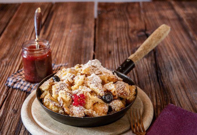 A warm dessert in a skillet with powdered sugar and berries, set on a rustic table near a cozy fire.