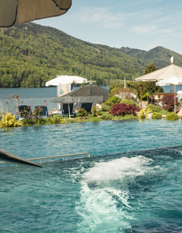 Poolside view with loungers and umbrellas, overlooking a scenic lake and lush green mountains in the background.