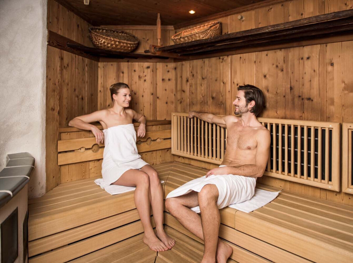 Two people relaxing in a cozy wooden sauna, wrapped in towels.