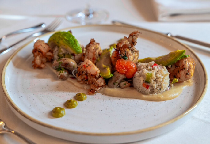 A gourmet seafood dish with shrimp, couscous, and vegetables artfully plated on a white dish.