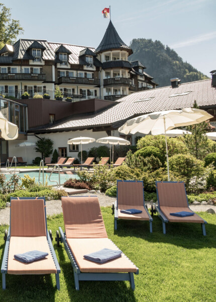 Luxurious hotel with sun loungers by a scenic outdoor pool, surrounded by lush greenery.