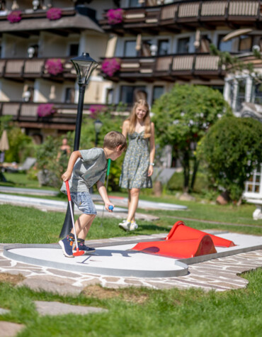Kinder spielen auf dem hoteleigenen Minigolf-Platz im Familienhotel Ebner's Waldhof am Fuschlsee.