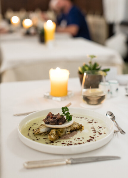 A gourmet dish elegantly plated on a white tablecloth with a lit candle in the background, creating a cozy dining ambiance.