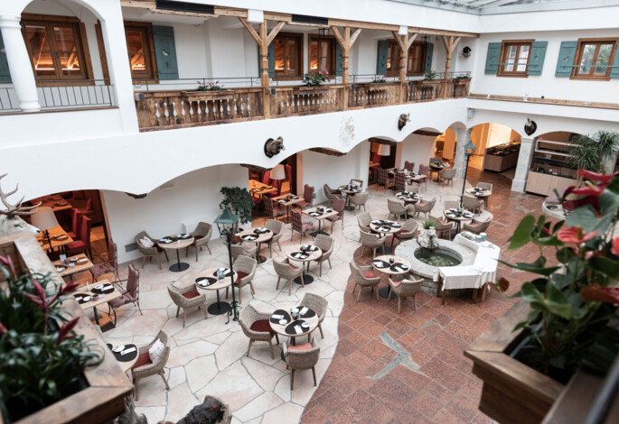 Spacious hotel atrium with elegant dining setup, surrounded by rustic decor and indoor plants.