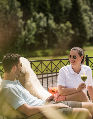 A couple relaxes outdoors with drinks, surrounded by a lush, scenic landscape.