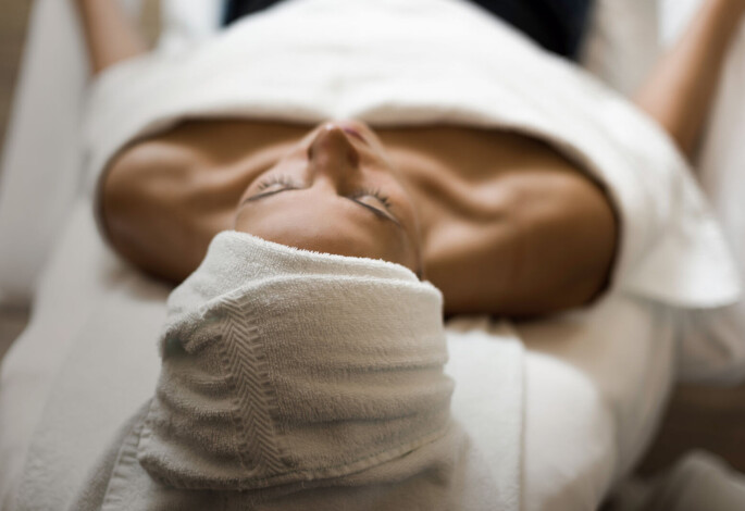 A person relaxing on a spa table with a towel wrapped around their head, creating a serene atmosphere.