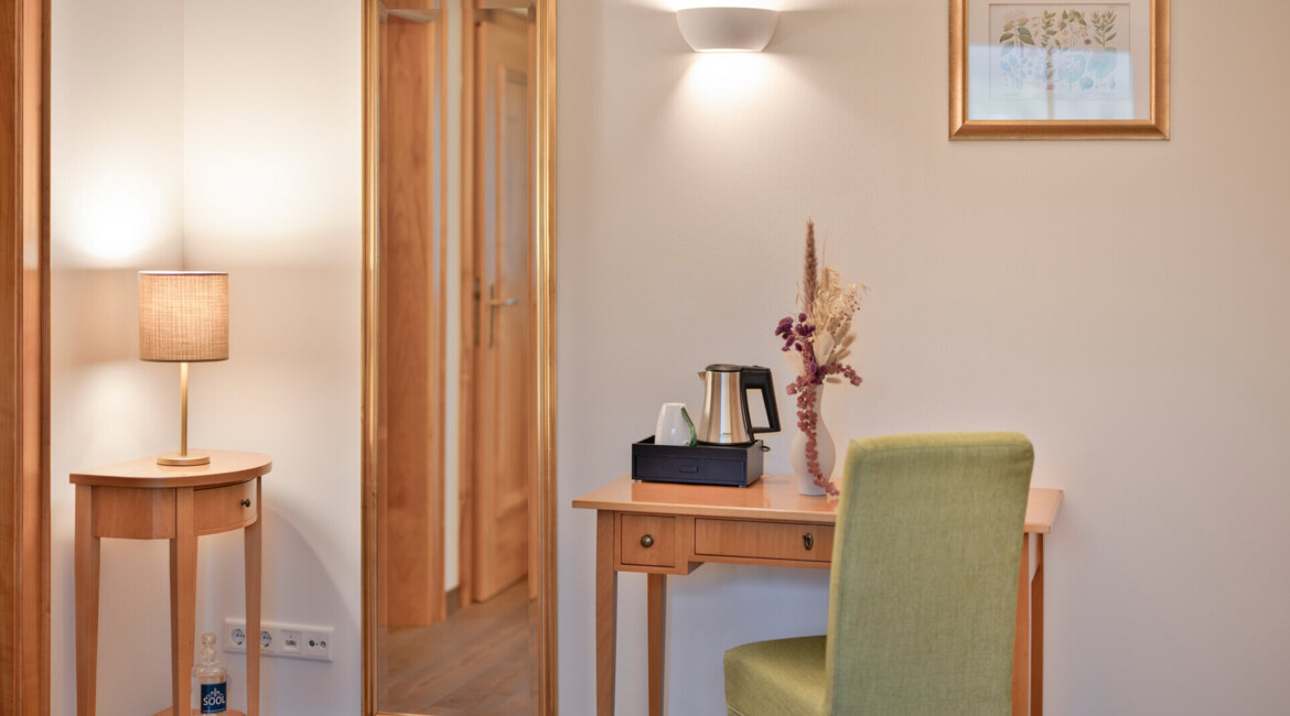 A cozy room with a wooden desk, green chair, mirror, and decorative lamp, creating a warm and inviting atmosphere.