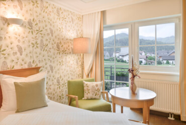 Cozy hotel room with floral wallpaper and a view of scenic mountains through a window.