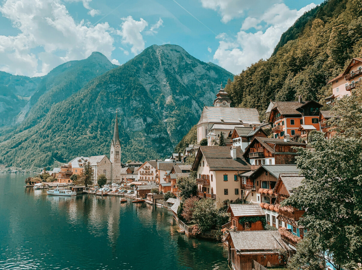 Bad Aussee village with charming buildings, a church spire, and lush mountains in the background under a blue sky.