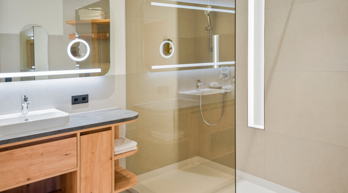 Modern bathroom with a glass shower, wooden cabinetry, and illuminated mirrors.