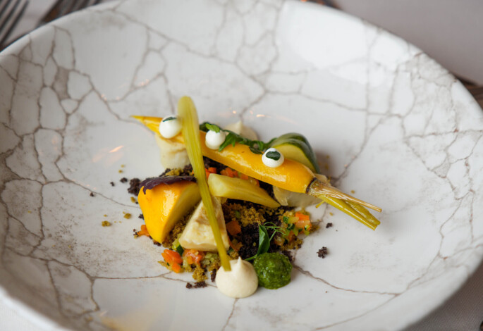 Elegant dish with colorful vegetables and artistic presentation on a marbled plate.