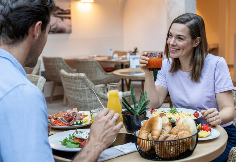 Zwei Personen genießen ein Frühstück mit frischen Säften, Gebäck und Omelett in einem gemütlichen Restaurant.