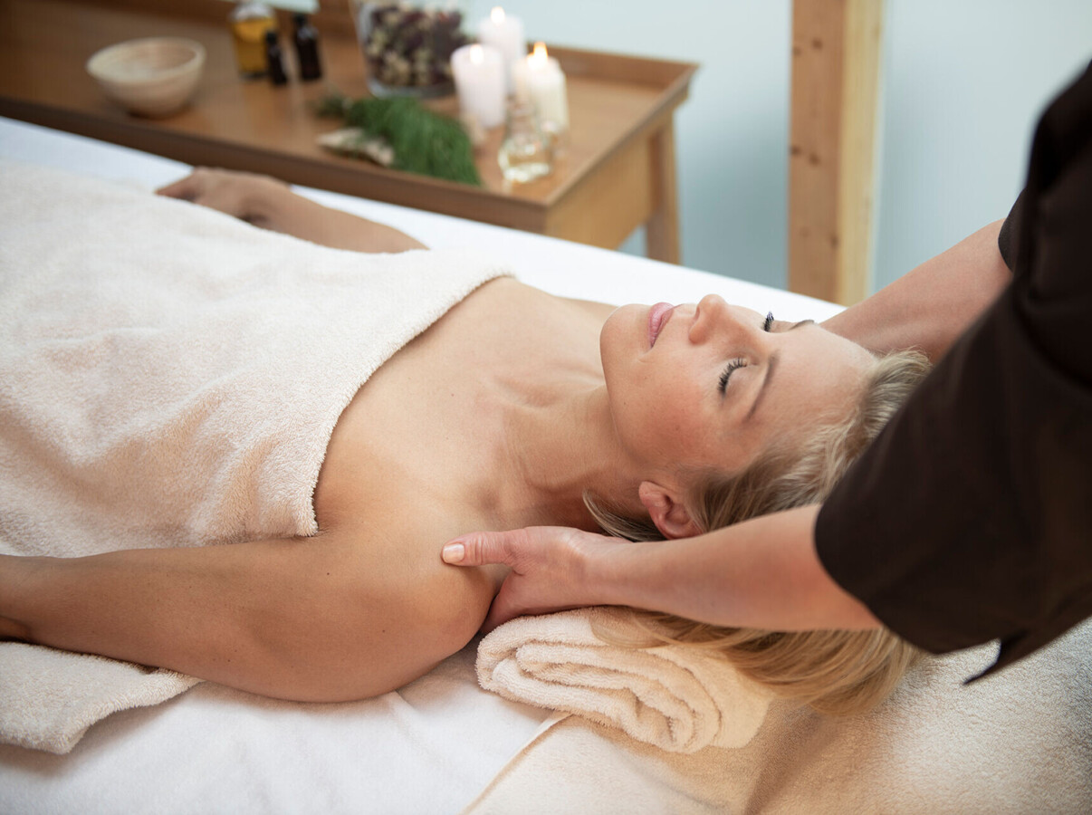 A person receiving a relaxing massage with candles and oils in the background.