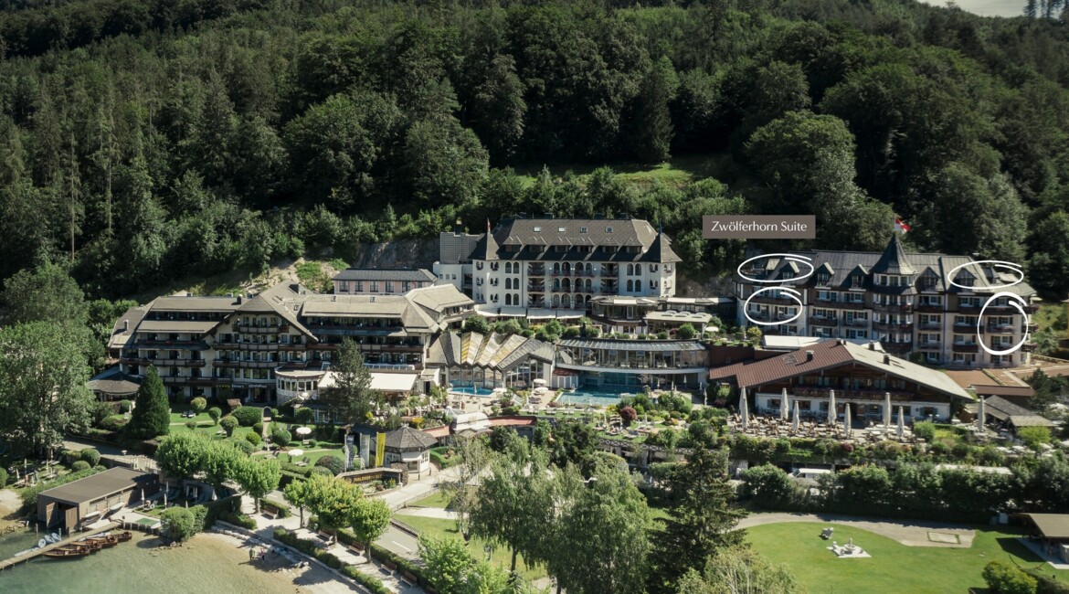 Aerial view of a scenic lakeside hotel surrounded by lush greenery, with labeled "Zwölferhorn Suite."