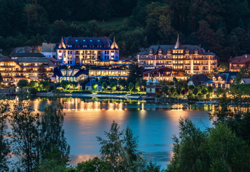 Der Waldhof Fuschlsee spiegelt sich bei Nacht im Fuschlsee, umgeben von Bäumen und Hügeln.