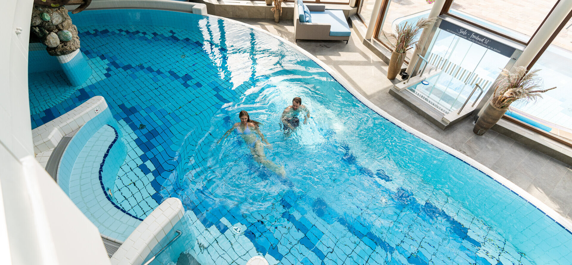 Ein Pärchen schwimmt im Indoor-Pool im Wellnesshotel Waldhof Fuschlsee Resort im Salzkammergut.