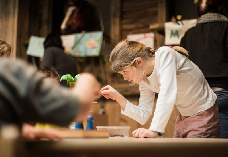 A girl focused on a tabletop activity, surrounded by other children in a classroom setting.