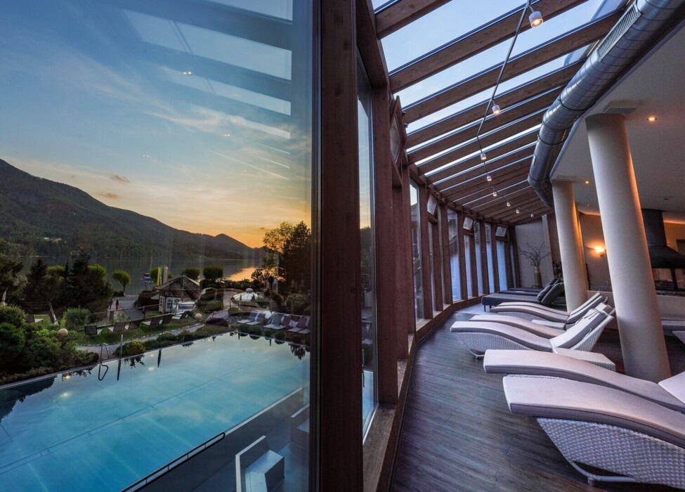 Scenic view from Waldhof Fuschlsee Resort's indoor pool area, overlooking Lake Fuschl and mountains at sunset.