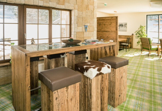 Cozy wooden bar area with high stools, featuring a plaid carpet and large windows overlooking a snowy landscape.