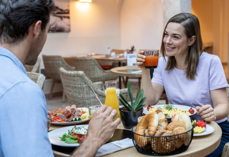 Zwei Personen genießen ein Frühstück mit frischen Säften, Gebäck und Omelett in einem gemütlichen Restaurant.