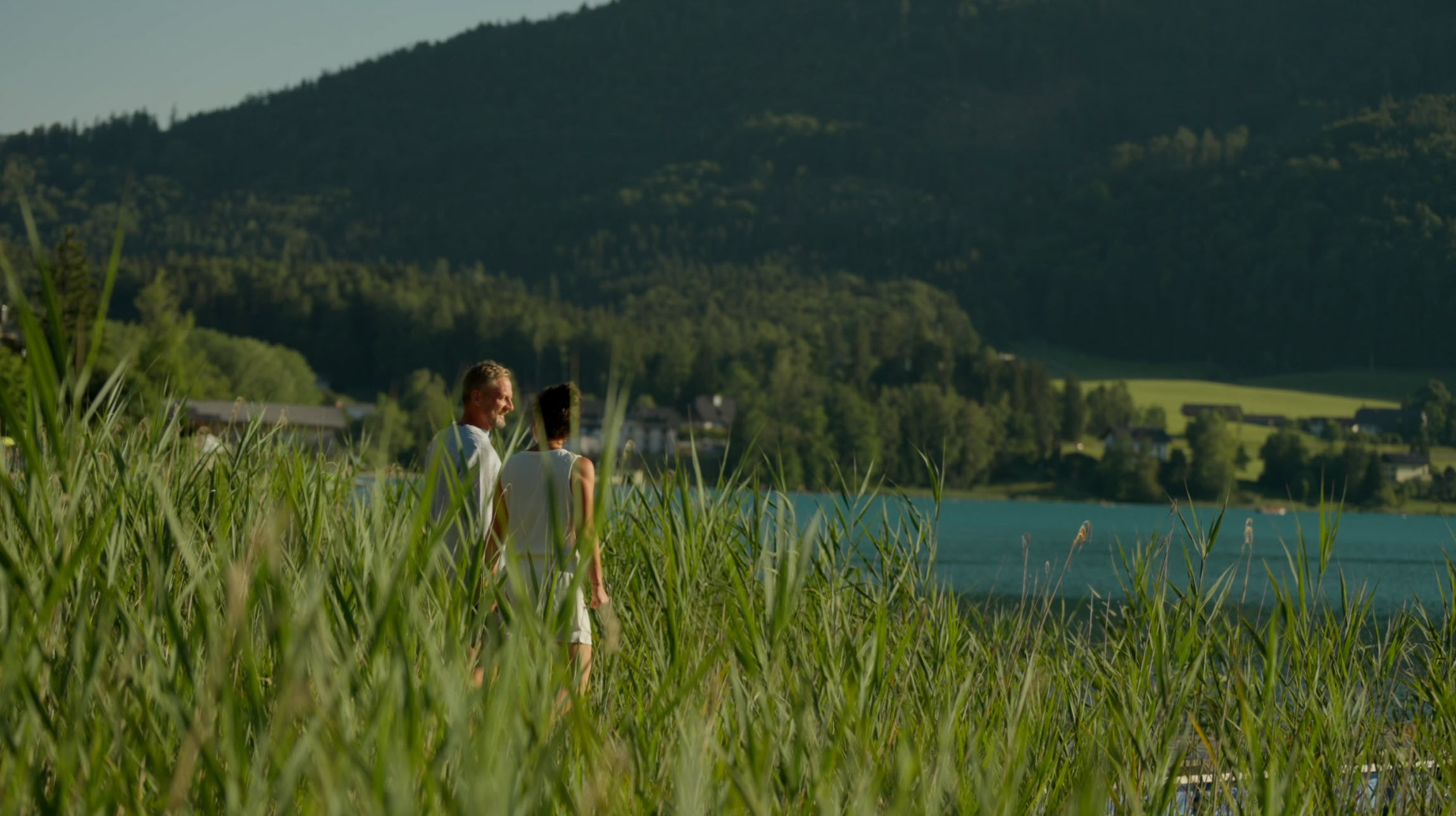 A couple enjoying the view of lake Fuschl surrounded by greenery and hills.
