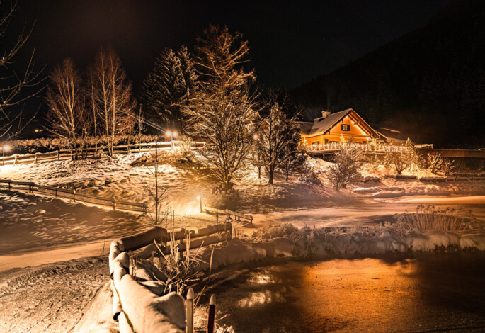 Die tief verschneite Waldhofalm im Winter bei Abendstimmung und beleuchteten Wegen.