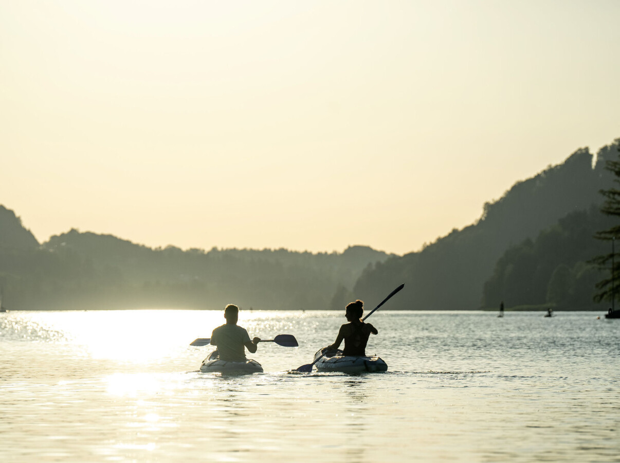 Two people kayaking on a tranquil lake at sunset, surrounded by scenic hills.