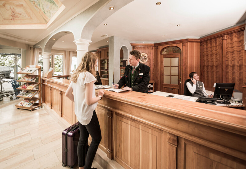 Woman checking in at hotel reception desk, with staff assisting and luggage nearby.