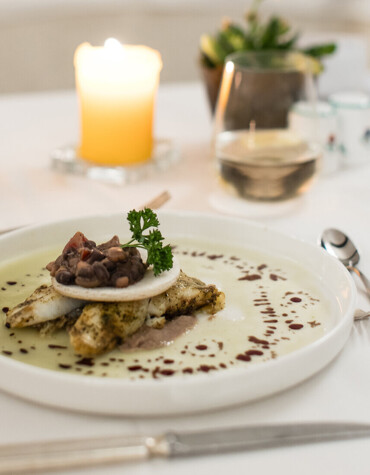 A gourmet dish elegantly plated on a white tablecloth with a lit candle in the background, creating a cozy dining ambiance.