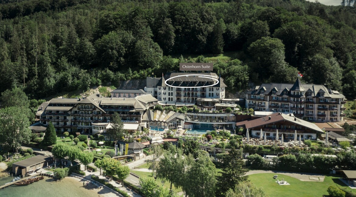 Aerial view of Waldhof Fuschlsee Resort with the Osterhorn Suite highlighted, surrounded by trees and near a lake.