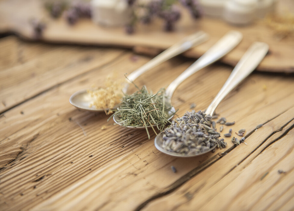 Drei Löffel mit getrockneten Kräutern, Lavendel und anderen Pflanzen auf einem Holztisch.