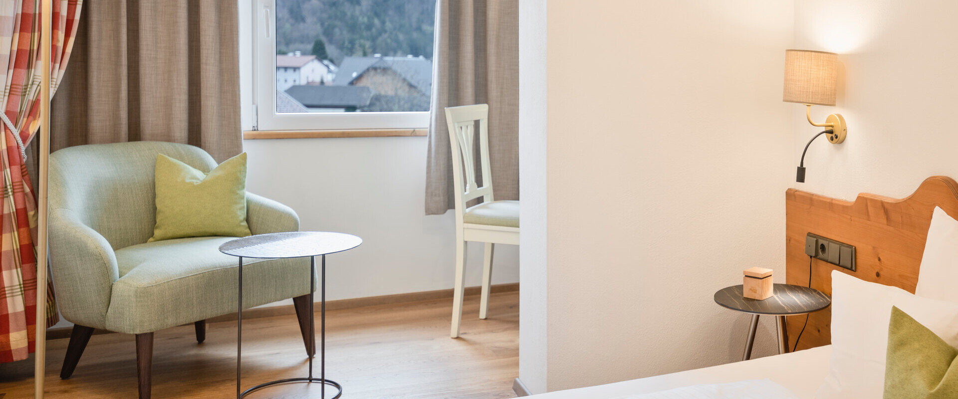 Bright hotel room with armchair, round tables, and a window view of mountains. Cozy ambiance with wooden accents and soft lighting.