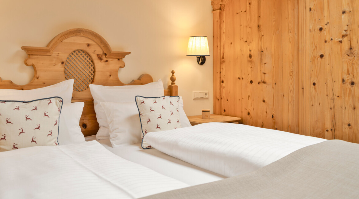 Cozy twin beds with decorated pillows and wooden headboard in a warmly lit room at Waldhof Fuschlsee Resort.