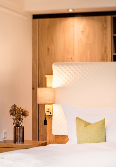 Hotel room with a cozy bed, green pillow, and soft lighting at Waldhof Fuschlsee Resort.