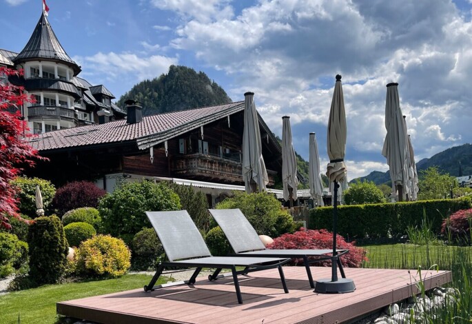 Two lounge chairs on a wooden deck in a lush garden with scenic mountain views in the background.
