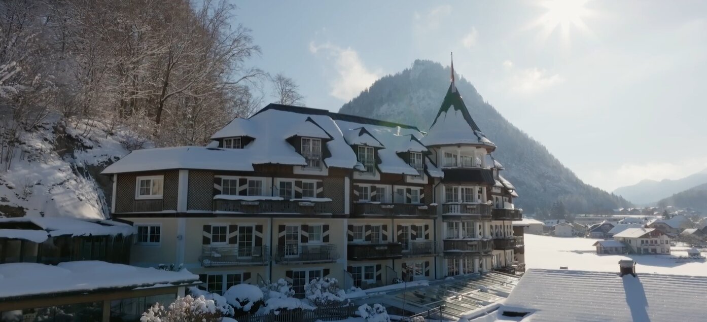 Snow-covered hotel with mountain backdrop under a clear sky.