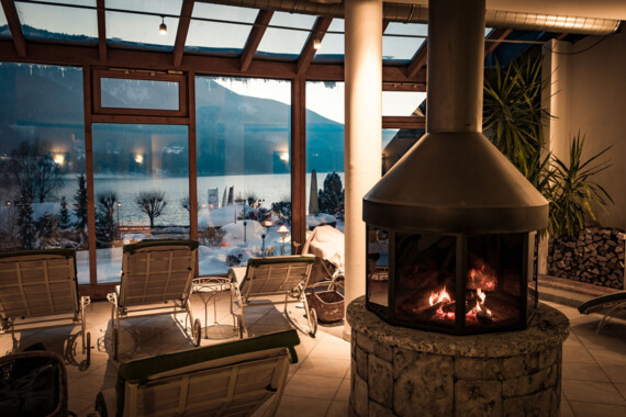 Cozy indoor lounge with a fireplace and scenic snowy lake view through large windows.