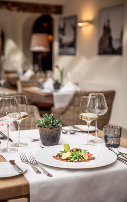 Elegant restaurant table setting with a gourmet dish, wine glasses, and a small plant, creating a cozy and inviting dining atmosphere.