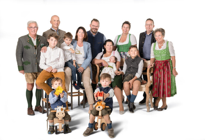 A family in traditional attire poses together, with children playing on wooden toys, against a plain background.