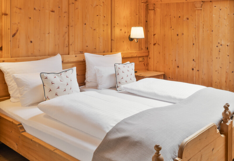 Hotelzimmer mit Holzverkleidung, Doppelbett mit weißen Kissen und Decken, weiches Licht von der Wandlampe.