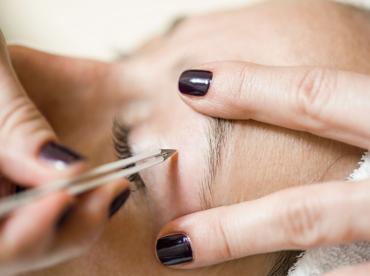 Eyebrow being carefully shaped with tweezers during a beauty treatment.