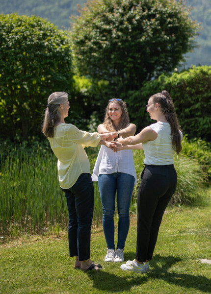 Drei Damen stehen im Kreis und halten sich an den Händen im Garten des Seminarhotel Waldhof Fuschlsee Resort.