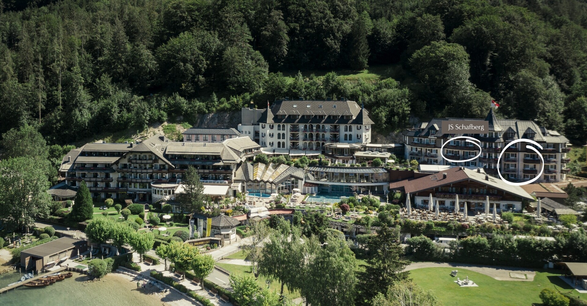 Luftaufnahme des Waldhofs am Fuschlsee, umgeben von Wald und See, mit mehreren Gebäuden und Grünflächen.