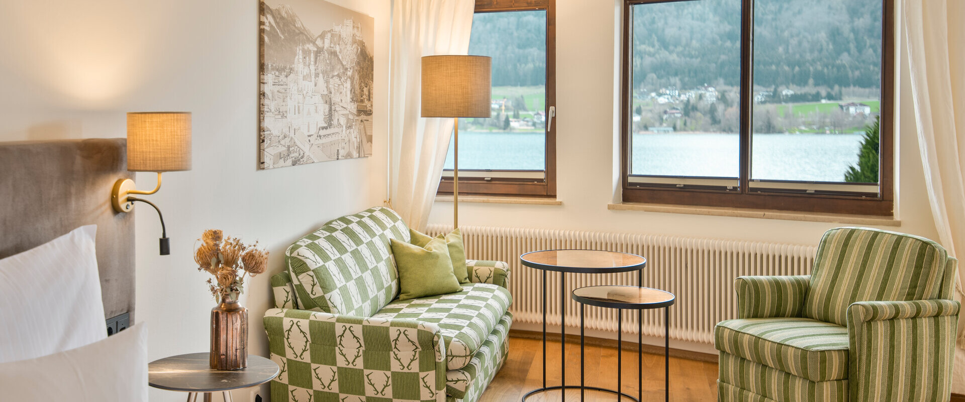 Hotel room at Waldhof Fuschlsee Resort with a lake view, featuring a green sofa, armchair, and elegant lighting.